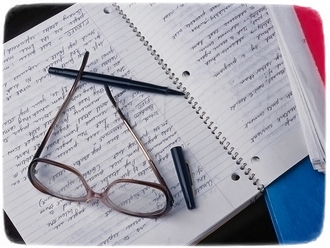 Na zdjęciu widać okulary i długopis znajdujące się na zapisanym zeszycie.